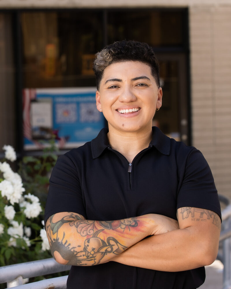 Vicky Alexandra Lopez smiling with arms crossed in a black polo, standing in front of the Veterans Success Center